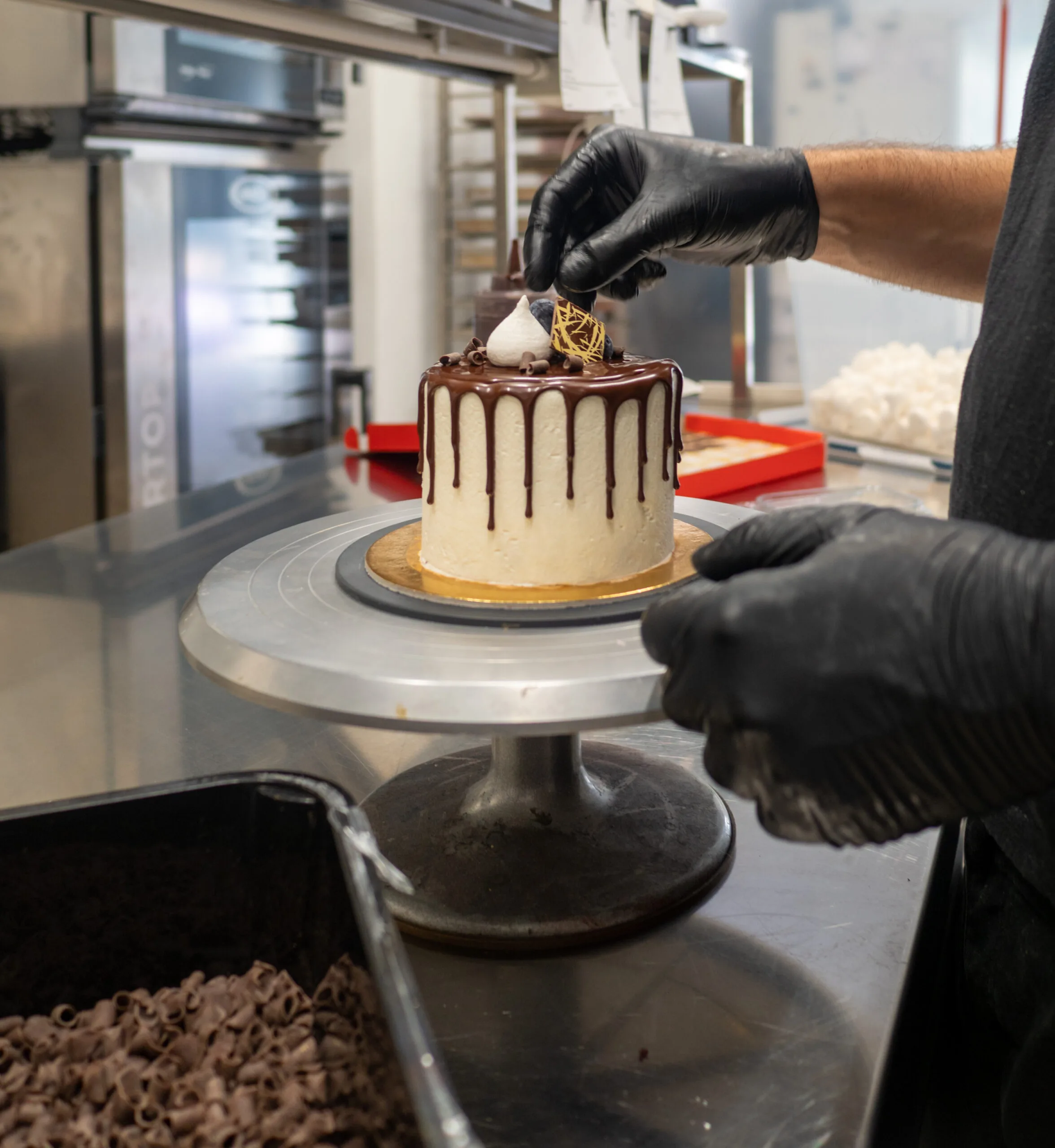 cake designer decorating a chocolate drip cake with mering and blueberries
